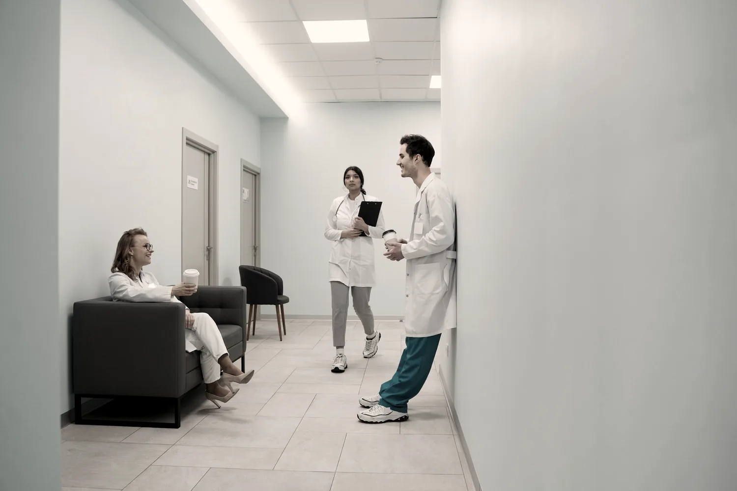Corridoio della clinica: un paziente in attesa e due operatori sanitari che si confrontano